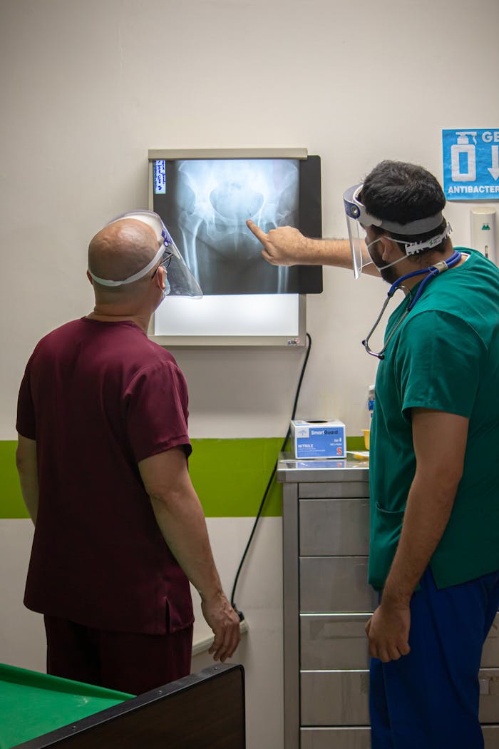 Two doctors wearing protective gear discuss a hip x-ray in a hospital room.